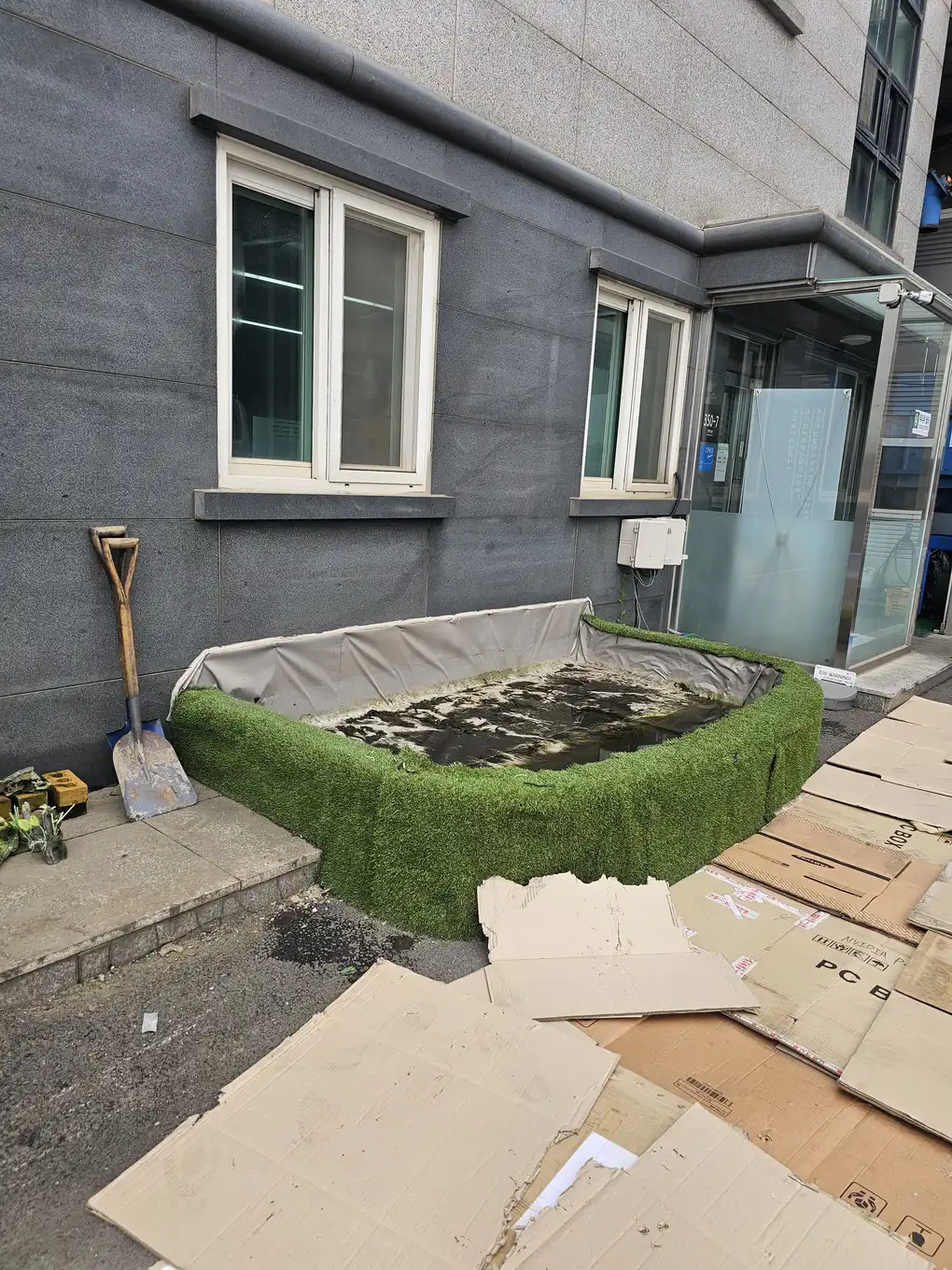 건물 입구 연못 리모델링 이전 잔디 매트로 감싼 구조물
